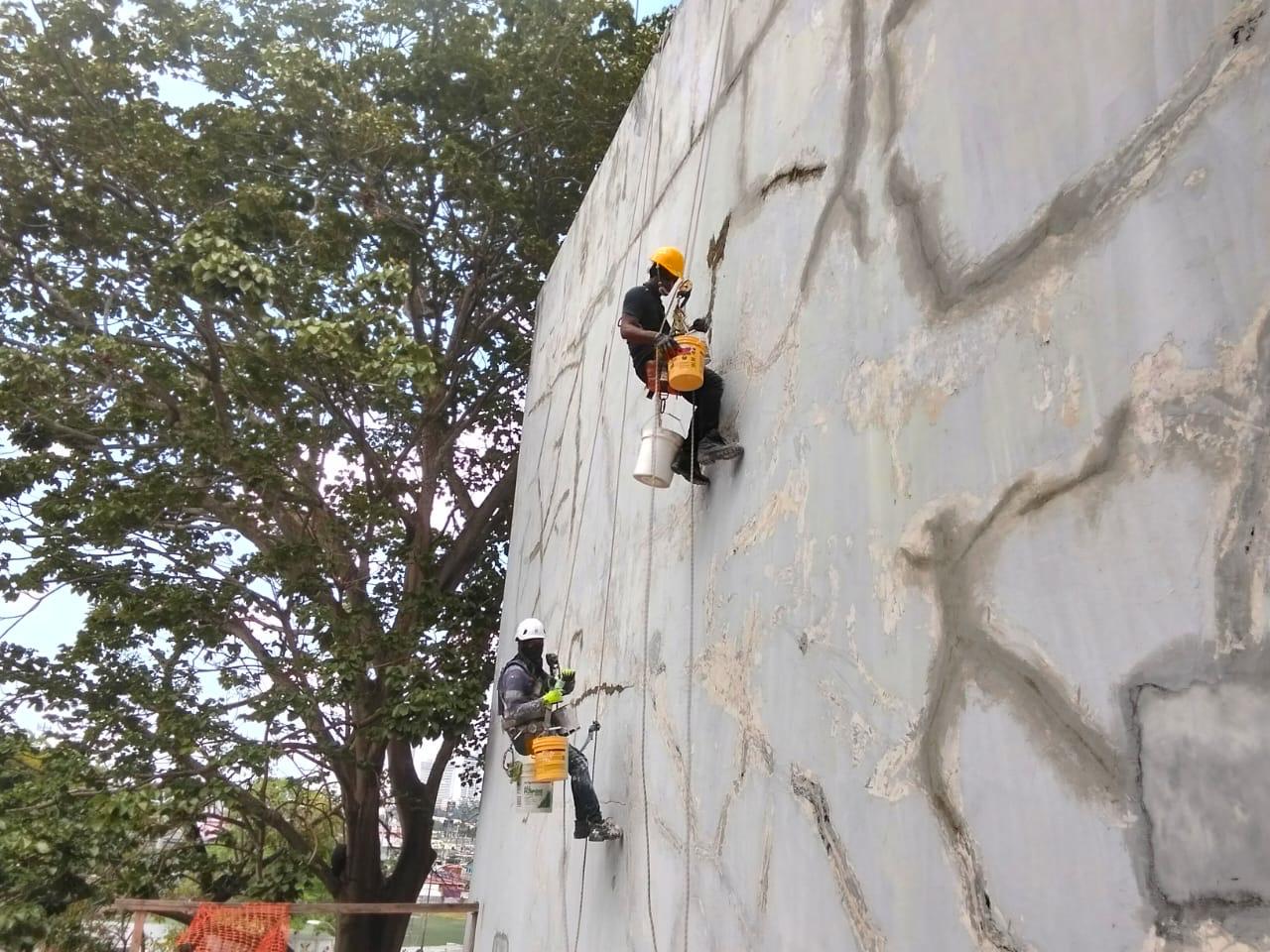 Técnicos trabajando con cuerdas en la pintura de una fachada